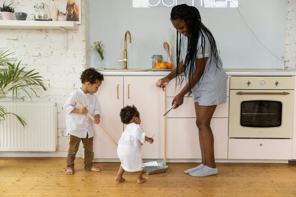 A mother and her two children cleaning together in a bright, modern kitchen.