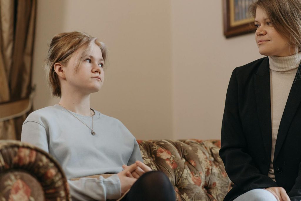 A mother and daughter sitting on a vintage floral sofa in a cozy indoor setting.