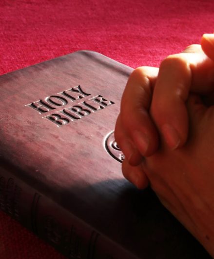 Close-up of hands praying on a Holy Bible, symbolizing faith and spirituality.